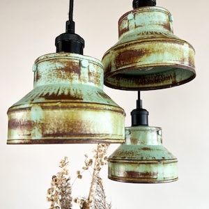 May include: Three rustic pendant lights with a distressed green finish and black cords. The lights have a unique, industrial style.