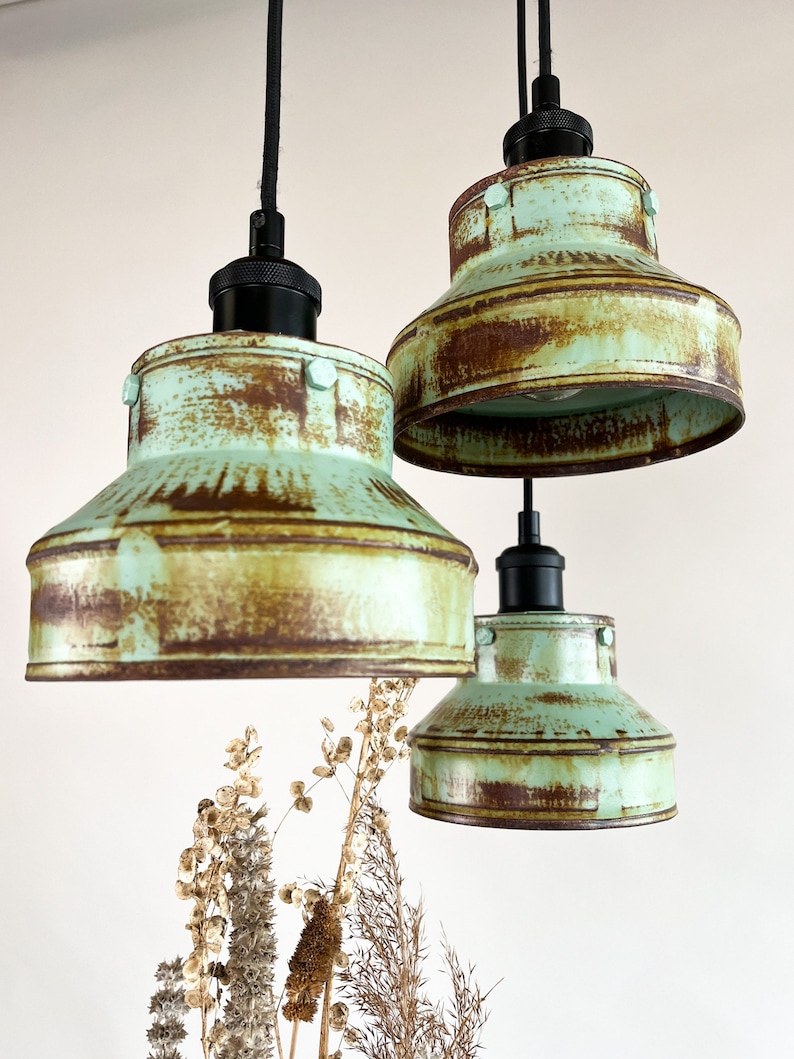 May include: Three rustic pendant lights with a distressed green finish and black cords. The lights have a unique, industrial style.
