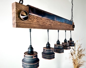 Op de afbeelding: Een rustieke houten plafondlamp met zes zwarte en koperen hanglampen. De houten balk is donkerbruin gebeitst en heeft een koperen metalen accent.