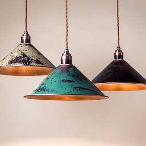 May include: Three pendant lights with cone-shaped shades in distressed finishes. One is green, one is black, and one is off-white. Each has a copper-colored interior and a brown cord.
