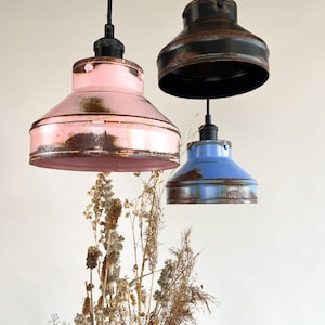 May include: Three pendant lights with distressed metal shades in pink, blue, and black. The shades have a rustic, vintage look.