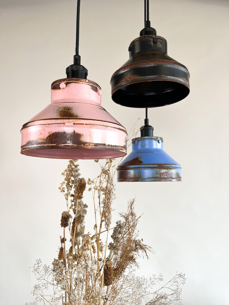 May include: Three pendant lights with distressed metal shades in pink, blue, and black. The shades have a rustic, vintage look.