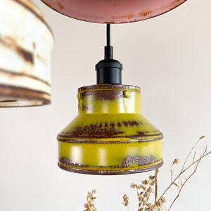 May include: A yellow metal pendant light fixture with a black cord and a black socket. The light fixture has a distressed finish and is hanging from the ceiling.