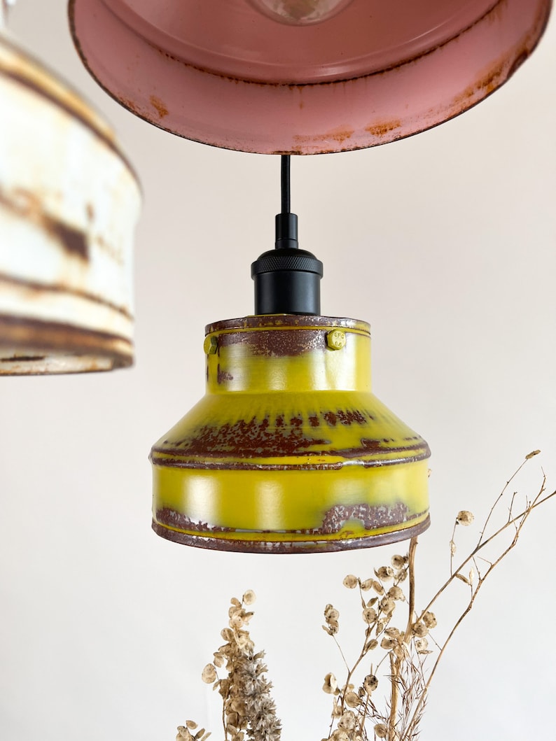 May include: A yellow metal pendant light fixture with a black cord and a black socket. The light fixture has a distressed finish and is hanging from the ceiling.