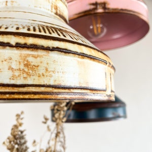 May include: Three vintage-style pendant lights with a rustic, distressed finish. The lights are in shades of white, pink, and blue.