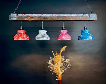 May include: A rustic, four-light pendant lamp with a wooden beam and metal accents. The lamp shades are painted in red, gray, pink, and blue. The fixture hangs from a chain, and a vase of dried flowers is in the foreground.