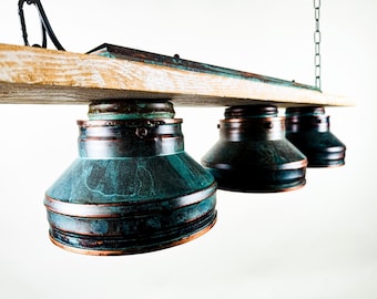 May include: A rustic, three-light pendant lamp with a weathered wood beam and three teal-colored metal shades. The shades have a distressed finish, and the fixture hangs from a chain. The wood beam is light-colored with dark accents.