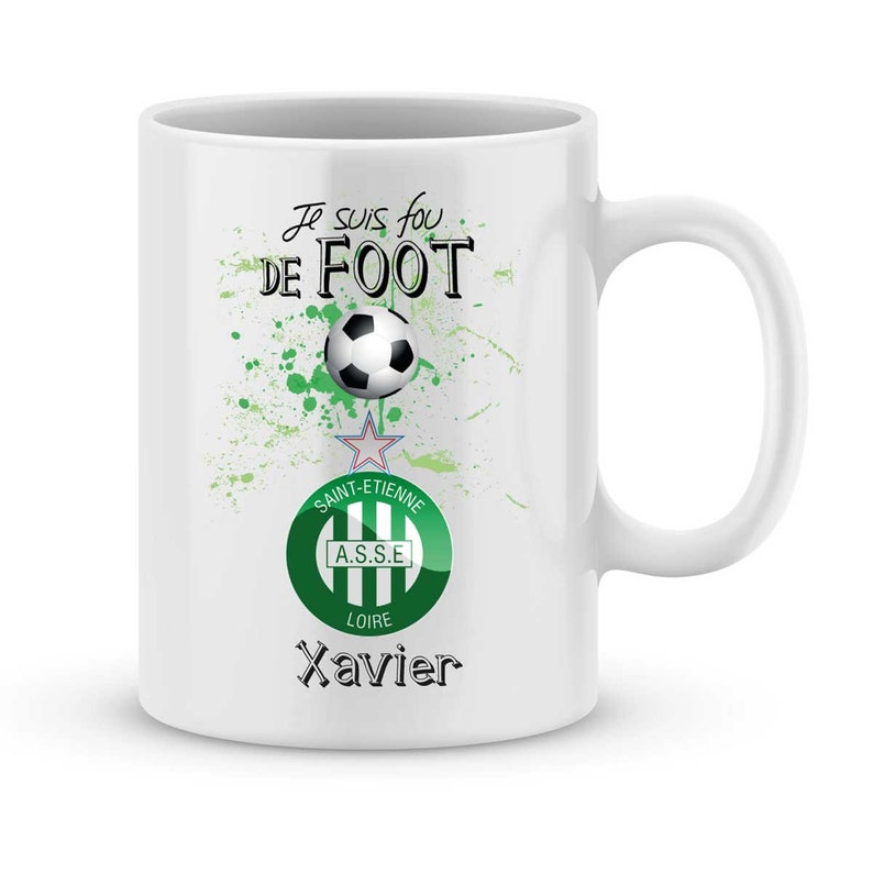 May include: White ceramic mug with a green and white soccer design. The mug has the text "Je suis fou de FOOT" and a soccer ball graphic. The design also includes a green and white soccer team logo with the text "SAINT-ETIENNE A.S.S.E. LOIRE" and the name "Xavier".