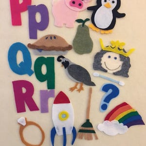 May include: Felt alphabet letters, numbers, and objects, including a pink pig, a penguin, a pear, a pie, a quail, a queen, a question mark, a rocket, a broom, a ring, a rainbow, and a cloud.