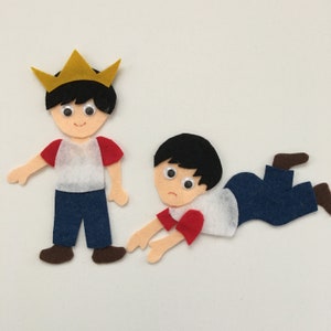 May include: Felt figures of two boys. One boy wears a gold crown and stands upright. The other boy is on the ground, looking sad. Both figures have black hair, red and white shirts, blue pants, and brown shoes.