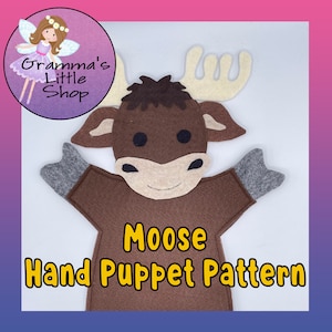 Puede incluir: Un patrón de marioneta de mano de fieltro marrón en forma de alce. La marioneta tiene orejas grandes y caídas, una nariz marrón y ojos negros. El texto "Moose Hand Puppet Pattern" está impreso en amarillo en el pecho de la marioneta.