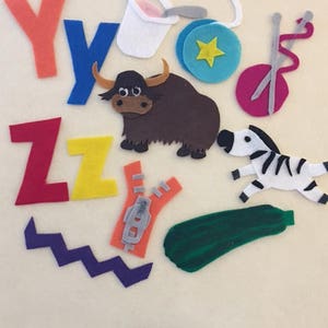 May include: Felt craft letters Y, Z, and Y, a brown yak, a green zucchini, a white yogurt container, a blue yo-yo, a pink yarn ball with two knitting needles, a purple zigzag, and a gray zipper.