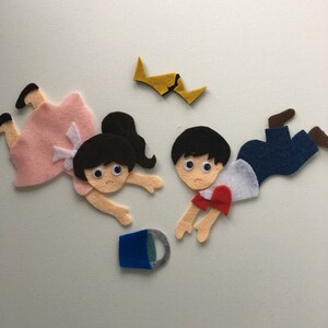 May include: Felt figures of two children and a broken yellow object, with a blue cup. The children have black hair and are wearing a pink dress, white shirt, red shirt, and blue jeans. The figures appear to be falling.