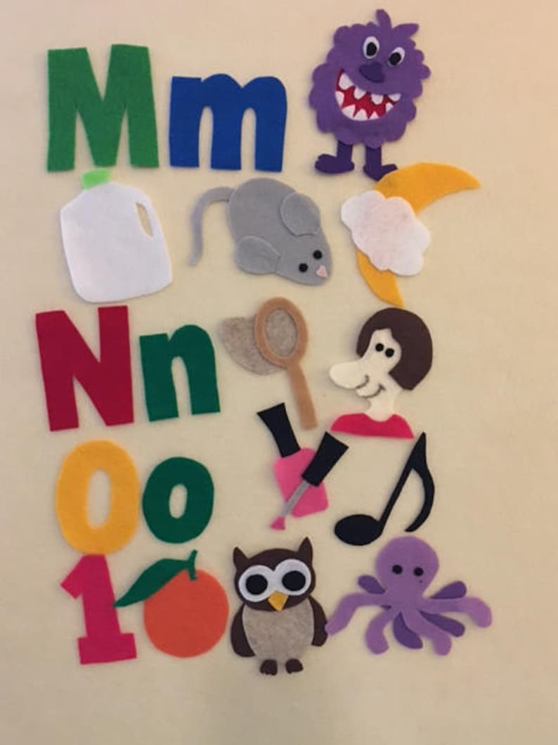 May include: Felt letter set for children, featuring the letters M, N, O, and a 1. The set includes various felt images, including a monster, a mouse, a milk carton, a net, a woman, a nail polish bottle, a musical note, an owl, an orange, and an octopus.