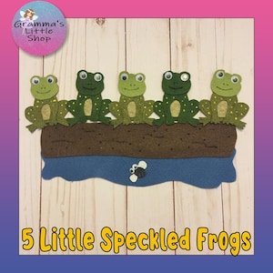 Può includere: Un artigianato in feltro con cinque rane verdi maculate sedute su un tronco marrone sopra l'acqua blu. Il testo "5 Little Speckled Frogs" è in basso. L'angolo in alto a sinistra ha un cerchio rosa e blu con il testo "Gramma's Little Shop".