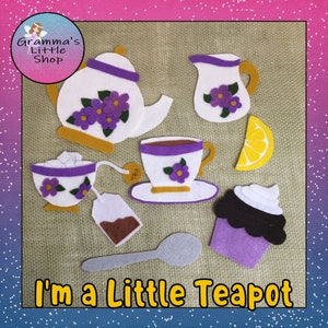 Può includere: Set da tè in feltro con una teiera, una tazza da tè, una zuccheriera, una brocca per la panna, una fetta di limone, un cupcake, un cucchiaio e una bustina di tè. Il set è viola, bianco e giallo con le parole "I'm a Little Teapot" in basso.