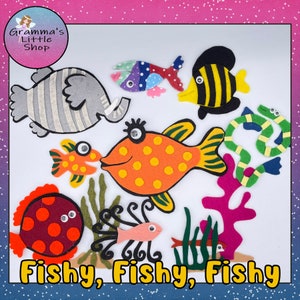 Może przedstawiać: Zestaw do rękodzieła z filcu z różnymi kolorowymi rybami, zielonym wężem, rafą koralową i słoniem. Zestaw zawiera słowa "Fishy, Fishy, Fishy" w żółtych literach.