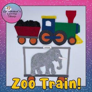 May include: A felt zoo train set featuring a colourful locomotive with a red smokestack, a coal car, and a grey cage car containing a grey felt elephant. A small white label above the elephant reads ELEPHANT, and the text ZOO TRAIN appears below.