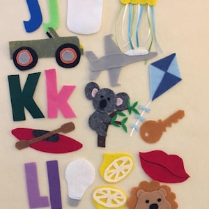 May include: Felt craft letters J, K, and L with various felt images including a green jeep, a white lightbulb, a red kayak, a yellow lemon, a blue kite, a brown key, a red lip, a brown lion, a grey koala, a grey airplane, a white jar with a red lid, and a pink jellyfish with blue tentacles.