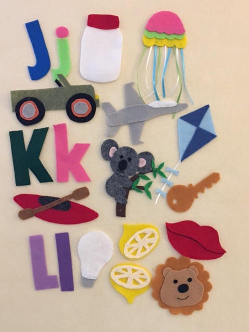 May include: Felt craft letters J, K, and L with various felt images including a green jeep, a white lightbulb, a red kayak, a yellow lemon, a blue kite, a brown key, a red lip, a brown lion, a grey koala, a grey airplane, a white jar with a red lid, and a pink jellyfish with blue tentacles.