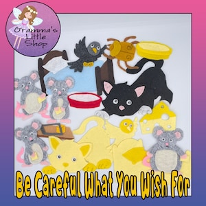Op de afbeelding: Een vilten speelset met een feeënlogo en de tekst "Gramma's Little Shop". De set bevat vilten muizen, een zwarte kat, een gele kat, een vogel, een bed, een kever, een kom, kaas en de tekst "Be Careful What You Wish For".