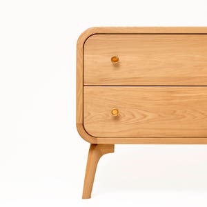 May include: A light wood dresser with two drawers and rounded edges. The dresser has brass knobs and sits on four legs.