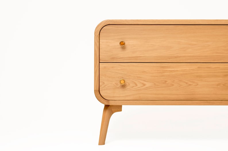 May include: A light wood dresser with two drawers and rounded edges. The dresser has brass knobs and sits on four legs.