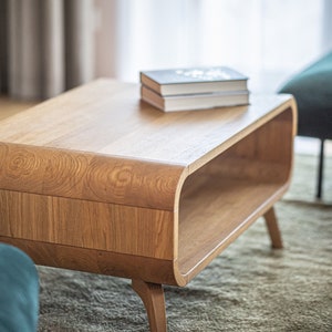 May include: A light wood coffee table with a curved, open shelf and rounded legs. The table has a stack of books on top.