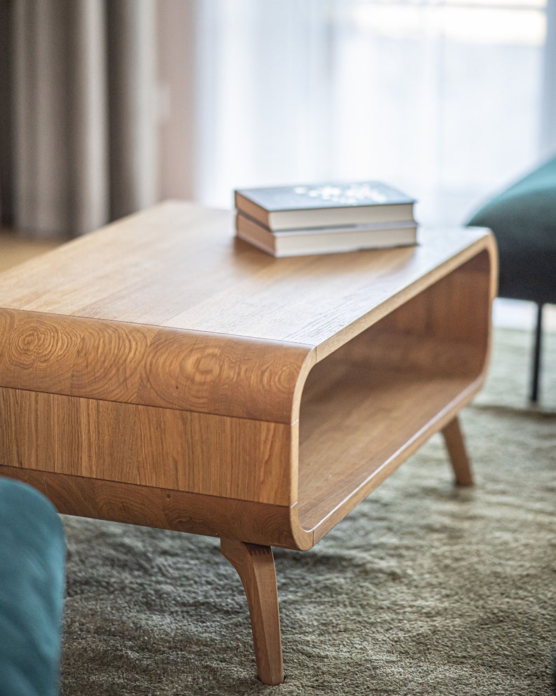 May include: A light wood coffee table with a curved, open shelf and rounded legs. The table has a stack of books on top.
