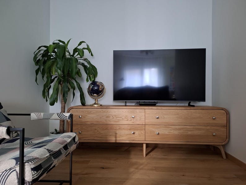 May include: A light wood entertainment center with four drawers and a curved front. A flat screen television is mounted above the entertainment center. A globe and a potted plant are on the left side of the entertainment center.