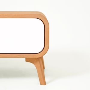 May include: A wooden cabinet with a white door and rounded edges. The cabinet has four legs and a simple design.
