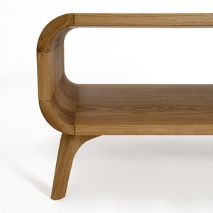 May include: A wooden coffee table with a curved design and a lower shelf. The table has a natural wood finish and four legs.