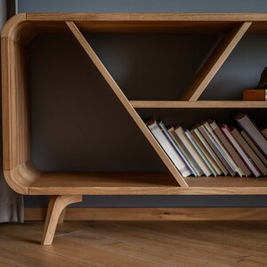 K&ouml;nnte beinhalten: Ein B&uuml;cherregal aus Holz mit einem einzigartigen geometrischen Design. Die Regale sind mit B&uuml;chern gef&uuml;llt und eine gr&uuml;ne Decke liegt auf dem obersten Regal.