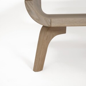 May include: A wooden bench with a curved back and four legs. The bench is made of light-colored wood and has a natural finish.