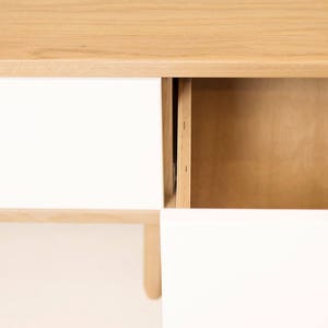 May include: A wooden cabinet with two drawers and a shelf. The drawers are white and the shelf is wood. The cabinet is on a white background.
