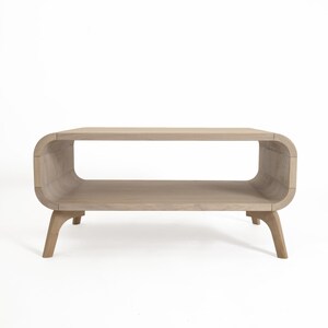 May include: A light wood coffee table with a curved, open shelf and four legs. The table has a modern design.