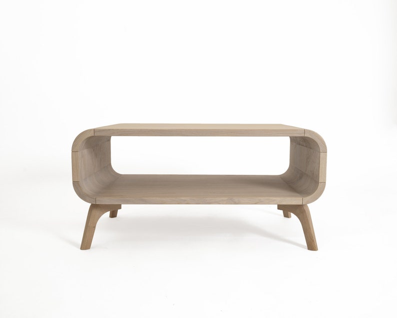 May include: A light wood coffee table with a curved, open shelf and four legs. The table has a modern design.