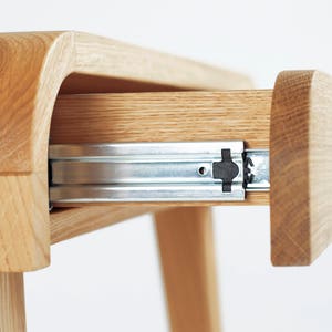 Puede incluir: Primer plano de un escritorio de madera con un caj&oacute;n parcialmente abierto. El escritorio es de madera clara, con vetas visibles. Los rieles del caj&oacute;n son met&aacute;licos. El escritorio tiene un dise&ntilde;o moderno y minimalista.