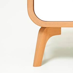 May include: Close-up of a white cabinet with rounded edges and wooden legs. The legs are a light brown color and have a curved design.