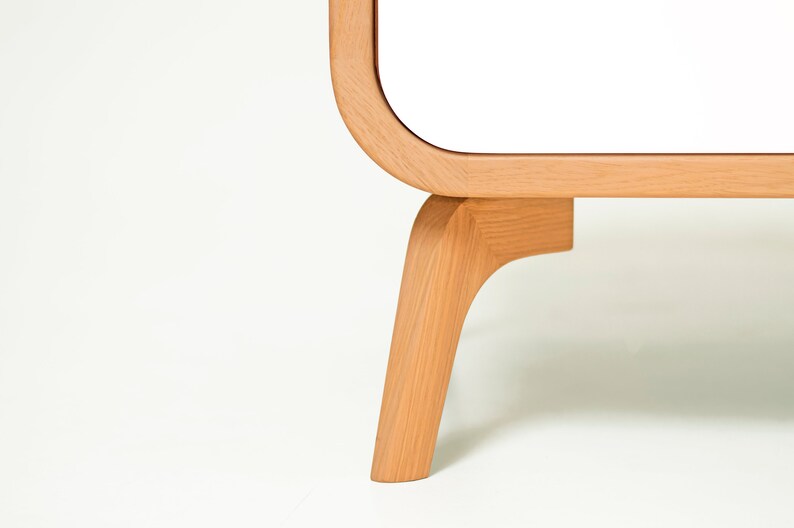 May include: Close-up of a white cabinet with rounded edges and wooden legs. The legs are a light brown color and have a curved design.