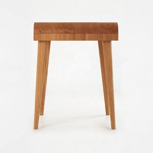 Puede incluir: Peque&ntilde;a mesa auxiliar de madera clara, con tapa curvada y cuatro patas anguladas. La madera, probablemente de roble, presenta un dise&ntilde;o minimalista y moderno. La mesa, de unos 60 cm de altura, es ideal para sal&oacute;n o dormitorio.