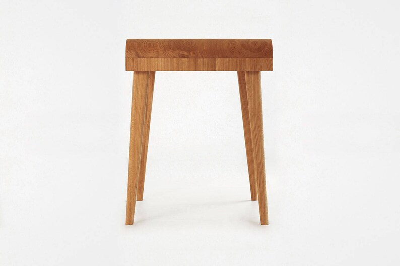 Puede incluir: Peque&ntilde;a mesa auxiliar de madera clara, con tapa curvada y cuatro patas anguladas. La madera, probablemente de roble, presenta un dise&ntilde;o minimalista y moderno. La mesa, de unos 60 cm de altura, es ideal para sal&oacute;n o dormitorio.