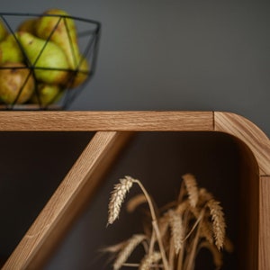 K&ouml;nnte beinhalten: Ein Holzregal mit einer abgerundeten Kante und einem dreieckigen Regal. Das Regal ist aus hellbraunem Holz gefertigt und hat eine nat&uuml;rliche Oberfl&auml;che. Das Regal ist leer, aber im Hintergrund befindet sich ein B&uuml;ndel getrockneter Weizenhalme.