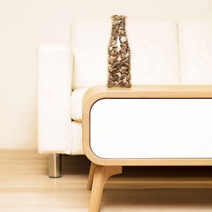 May include: A white couch with a wooden side table. The table has a white drawer and a clear glass bottle filled with small stones.