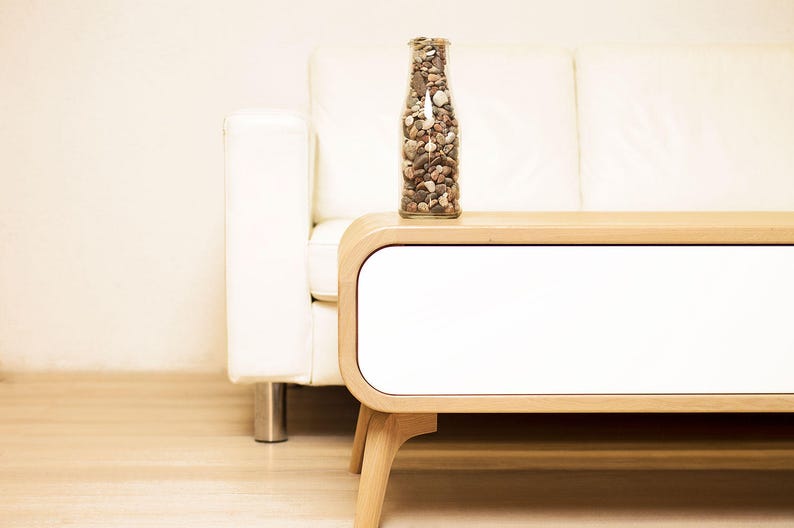 May include: A white couch with a wooden side table. The table has a white drawer and a clear glass bottle filled with small stones.