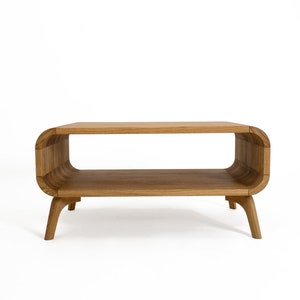 May include: A wooden coffee table with a curved, oval-shaped top and two shelves. The table has four legs that are slightly curved.