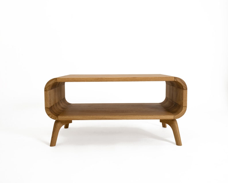 May include: A wooden coffee table with a curved, oval-shaped top and two shelves. The table has four legs that are slightly curved.