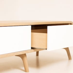 May include: A white and natural wood coffee table with two drawers. One drawer is open, revealing the natural wood interior.
