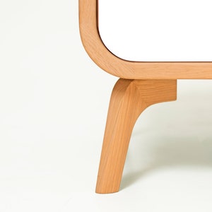 May include: Close-up of a white cabinet with rounded edges and wooden legs. The legs are a light brown color and have a curved design.