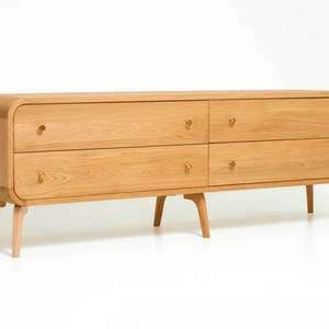 May include: A light wood dresser with four drawers and rounded edges. The dresser has four legs and brass knobs.